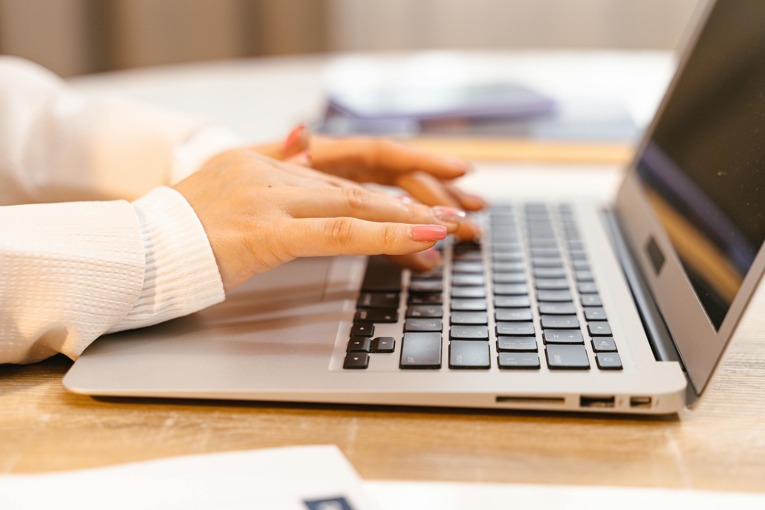 A close-up view of hands typing on a laptop keyboard with a focus on manicured nails and technology.