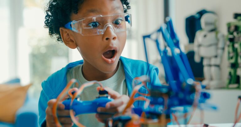 Closeup of Young African-American boy using remote control for robotics project amidst various technological tools and models at home. STEM Education robotics courses online concept.